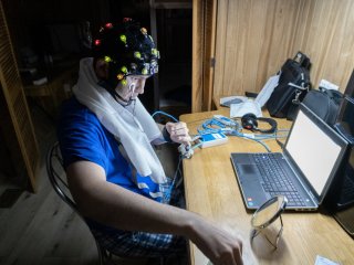 Участник эксперимента SIRIUS-23 Рустам Зарипов готовится к записи электроэнцефалограммы, для чего самостоятельно проверяет качество прилегания контактов (зеленое свечение — правильно, красное — нет). Фото из архива ИМБП РАН